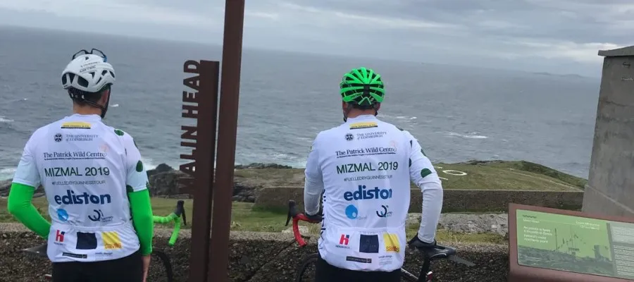 Two men in cycling helmets look out to sea. 