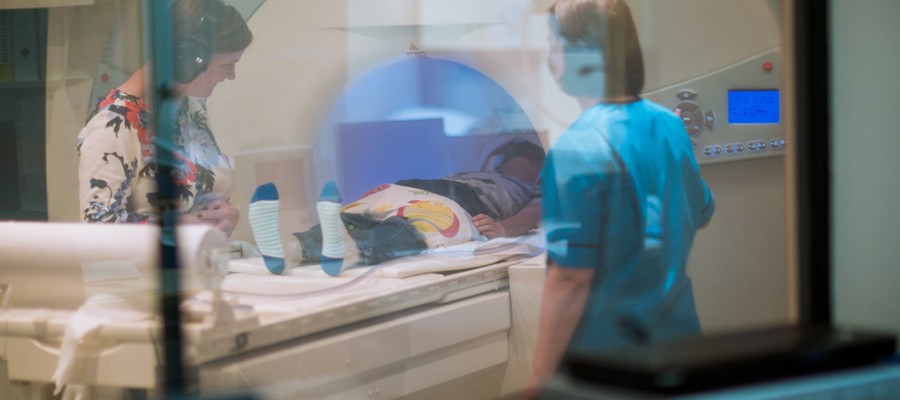 Child going into brain scanning machine while medical professional and carer supervise. 