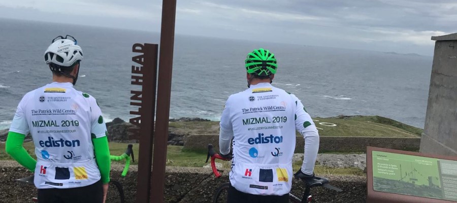 Two men in cycling helmets look out to sea. 